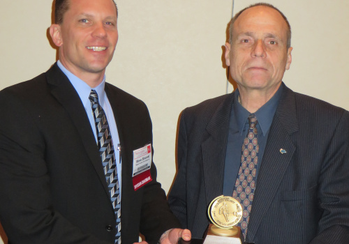 M. Chiesa reçoit le prix de M. Steve Sikorski, directeur de la division aluminium de l’AFS. L'AFS, American Foundry Society, a été fondé en 1896. Elle a pour mission de diffuser et promouvoir l'information entourant l'industrie des métaux. Elle compte 9000 membres répartis dans 47 pays.