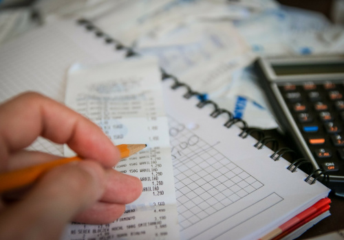 Un homme tenant un crayon, une facture, un cahier spirale et une calculatrice