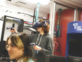 Une personne debout a un casque de réalité virtuelle derrière une personne assise