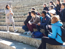 Un groupe de personnes écoutent une guide dans un auditorium extérieur