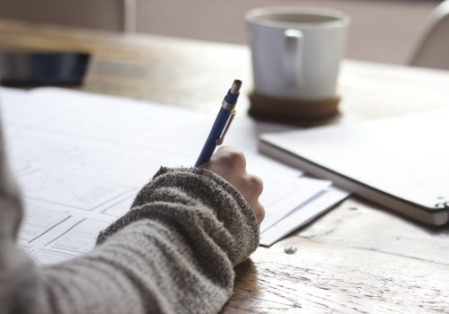 Un étudiant écrit, devant lui une tasse de café et un livre