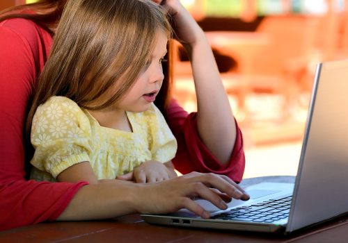 Une fillette assis sur les genoux de sa mère regarde un écran d'ordinateur