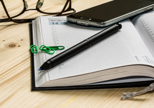 Sur une table, un agenda, un crayon, un téléphone portable et des lunettes